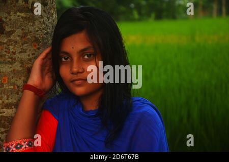 Nahaufnahme eines Teenagers, das einen Baum hält und in einem Reisfeld von Westbengalen in Indien lächelt, selektive Fokussierung Stockfoto