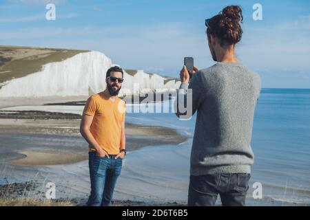Rückansicht von unkenntlich trendy Kerl Foto von männlich Bärtiger ethnischer Freund, während der Urlaub zusammen vor Kreidefelsen der Sieben Si Stockfoto