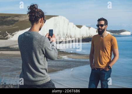 Rückansicht von unkenntlich trendy Kerl Foto von männlich Bärtiger ethnischer Freund, während der Urlaub zusammen vor Kreidefelsen der Sieben Si Stockfoto