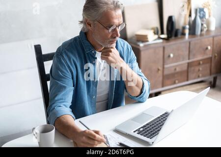 Mann mittleren Alters, der von zu Hause aus auf einem Laptop arbeitet. Stockfoto
