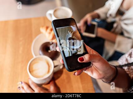 Von oben von unerkennbaren weiblichen mit Smartphone Aufnahme von Cappuccino und süßes Dessert am Tisch im Café Stockfoto