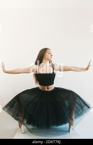 Anmutige weibliche Balletttänzerin trägt schwarze Tutu stehen in pointe Schuhe auf Zehenspitzen in Tanzposition auf weißem Hintergrund und Wegschauen Stockfoto