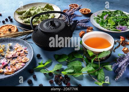 Kräutertee, natürlich, Bio und gesund. Eine Teetasse, eine Kanne und viele Kräuter, Früchte und Blumen auf blauem Hintergrund Stockfoto
