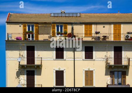 Fassade eines Mehrfamilienhauses in Savona, Italien. Gelbes Gebäude mit Fensterreihen und Balkonen. Stockfoto