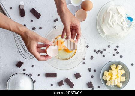 Draufsicht Zusammensetzung der Ernte anonyme Person bricht Eier in Schüssel mit verschiedenen Zutaten zum Backen auf den Tisch gelegt Stockfoto