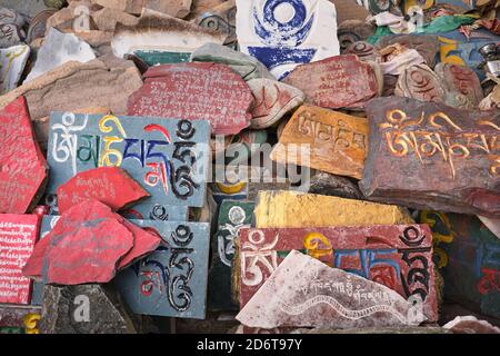 Ansicht des Sanskrit Mantra Om mani Padme Hum, eingraviert auf der schäbigen Oberfläche von mehrfarbigen Steinplatten bei Tageslicht Stockfoto