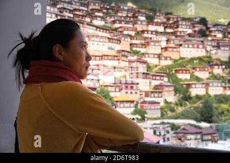 Seitenansicht der nachdenklichen erwachsenen ethnischen weiblichen Touristen in ungezwungener Atmosphäre Kleidung mit festgebundenen Haaren stehend mit aufgefalteten Armen Geländer und wegschauen Stockfoto