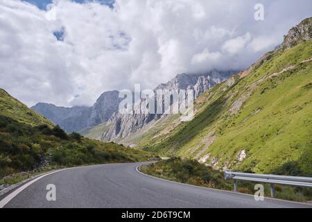 Kurviger Asphaltweg führt durch grasbewachsene Hügel mit Moos bedeckt Fast ruhige Gipfel verschwinden in der Ferne Stockfoto