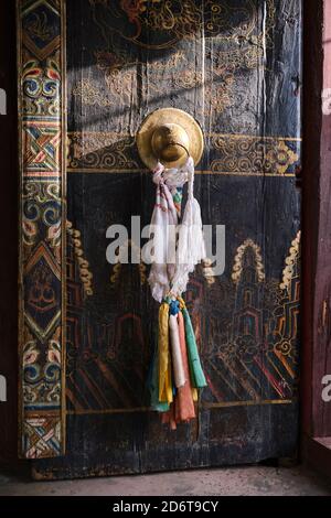 Teil eines alten tibetischen Gebäudes mit bemaltem Holztor In verschiedenen Ornamenten mit goldenem Griff mit rituellen Bändern Stockfoto