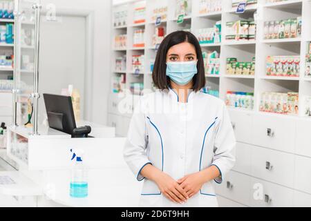 Junge türkische Apothekerin mit medizinischer Maske, die davor steht Der Theke in der Apotheke Stockfoto