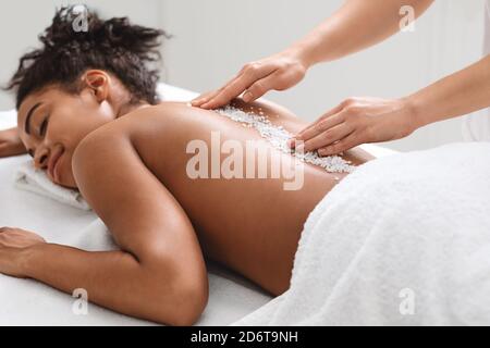 Fröhliche schwarze Dame bekommen heilende Salzmassage im modernen Spa Stockfoto