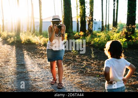 Nicht erkennbare junge Fotografin in legerer Kleidung und Hutschussen Bezaubernder kleiner Sohn, der auf einer Gasse im malerischen Park steht Stockfoto