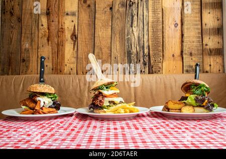 Verschiedene appetitliche Burger mit Gemüse und Kotelett auf Teller mit Kartoffeln auf dem Tisch im rustikalen Café serviert Stockfoto