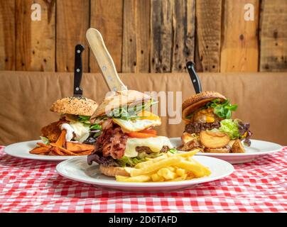 Verschiedene appetitliche Burger mit Gemüse und Kotelett auf Teller mit Kartoffeln auf dem Tisch im rustikalen Café serviert Stockfoto