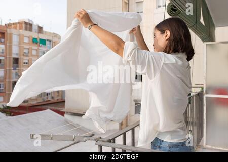 Seitenansicht der jungen Frau in weißem Hemd und Jeans Hängen Wäsche auf Wäscheleine auf dem Balkon Stockfoto