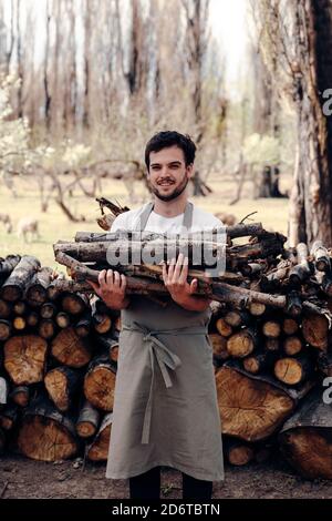 Mann in der Schürze, der Holz aus dem Holzstapel im Wald für ein Picknick abnahm Stockfoto