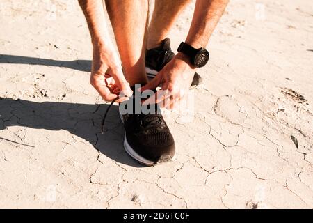 Von oben der Ernte anonymen männlichen Athleten binden Schnürsenkel auf Turnschuhe während der Vorbereitung für das Training in der trockenen Wüste auf sonnigen Tag Stockfoto