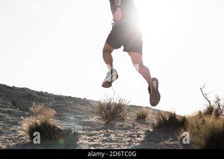 Rückansicht von Crop anonymous männlichen Läufer in Sportbekleidung springen Auf verlassenen hügeligen Gelände während des morgendlichen Trainings Stockfoto