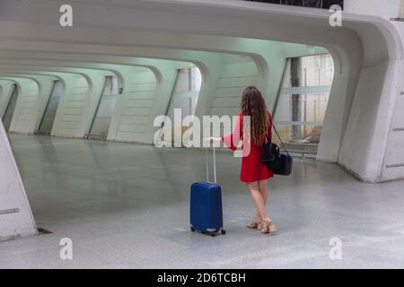 Rückansicht einer anonymen Frau in rotem Kleid, die mit dem Koffer im Flughafengang läuft Stockfoto