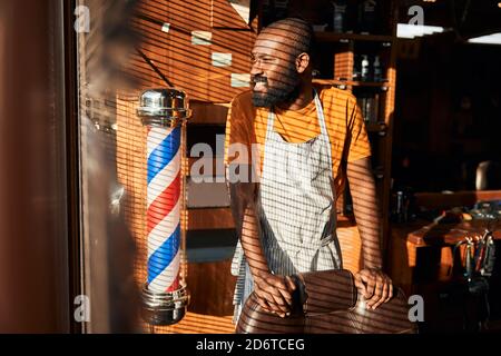 Bärtiger afroamerikanischer Mann, der im Friseurladen am Fenster steht Stockfoto
