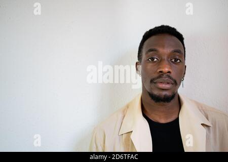 Nachdenkliche junge afroamerikanische männlich in hellbeige formelles Hemd Rücksichtsvoll wegschauen, während man in der Nähe einer weißen Wand steht Stockfoto