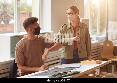 Warm getönte Porträt von zwei Kollegen tragen Masken stoßen Ellbogen Als kontaktlose Begrüßung im Post-Pandemie-Büro Stockfoto