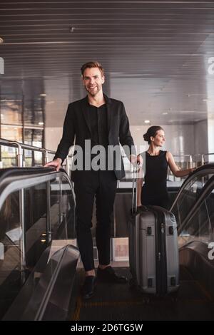 Mann und Frau tragen ihren Koffer durch die Rolltreppe Stockfoto