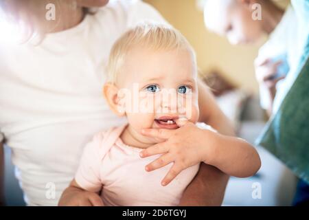 Crop Frau umarmt niedlichen Baby Tochter saugen Finger beim Ausruhen auf weichen Couch zu Hause Stockfoto