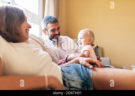 Voller Körper der fröhlichen Mutter sitzt auf der Couch mit Mann Und spielen mit Baby im gemütlichen Wohnzimmer Stockfoto