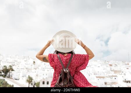 Rückansicht von anonymen stilvollen Touristen mit Strohhut und Erhöhte Arme betrachten alte Häuser in Rhodos unter bewölktem Himmel Stockfoto