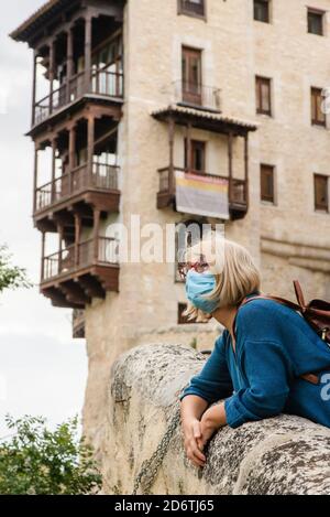 Flache Seitenansicht einer Reisenden Frau in Schutzmaske, die sich an einer Steingrenze in der Nähe eines alten Gebäudes lehnt und beim Besuch der mittelalterlichen Stadt Cue wegschaut Stockfoto