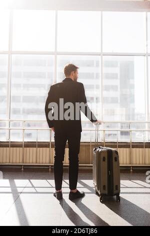 Mann, der mit einem Koffer neben dem riesigen Fenster steht Stockfoto