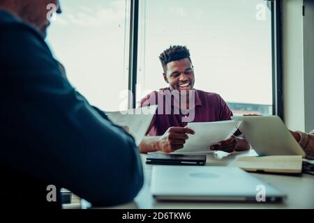 Männlicher Geschäftsmann, der lachend mit Kollegen über Punkte diskutiert Zur Verbesserung der Geschäftsabläufe Stockfoto