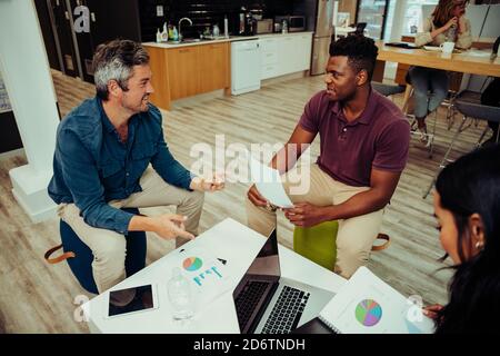 Gemischter Renner, der sich auf ein Interview mit kaukasischem Kollegen vorbereitet In der Lounge am Arbeitsplatz Stockfoto
