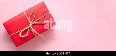 Rote Geschenkbox mit Garn auf einem hellrosa Hintergrund gebunden. Banner. Urlaubskonzept. Weihnachten, Muttertag, Valentinstag, Internationaler Frauentag Stockfoto