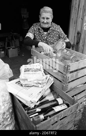 15. November 1984, Sachsen, Eilenburg: In einer Sammelstelle für Sekundärrohstoffe des VEB Kombinat Sekundär-Rohstofferfassung (SERO) - Zeitungssammlung; Pappe; Altpapier; Flaschen, Gläser, Lumpen; Metallschrott - eine ältere Frau steht im November 1984 hinter festgebundenen Bündeln von Tageszeitungen und Kisten mit Alkoholflaschen. Genaues Aufnahmedatum nicht bekannt. Foto: Volkmar Heinz/dpa-Zentralbild/ZB Stockfoto