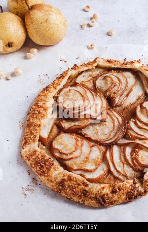 Frisch gebackene Birne- und Haselnusspraline-Galette mit frischen Birnen und gehackten Haselnüssen im Hintergrund. Stockfoto