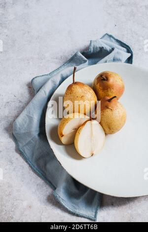 Herbstlicher Teller mit frischen Birnen auf einer blauen Serviette mit einer in zwei Hälften geschnittenen Birne. Stockfoto