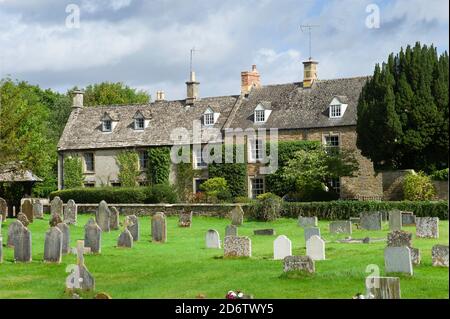 Dorf Kingham im Cotswold mit malerischen Kalksteinhäusern und Grabsteine auf dem Friedhof und blauer Wolkenhimmel Stockfoto