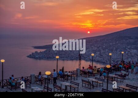 Saranda/Albanien – 1. August 2020: Luftpanorama Stadtbild auf Sonnenuntergang, Meer, Berge, bunten Himmel, Outdoor-Café und Menschen, genießen die Aussicht Stockfoto