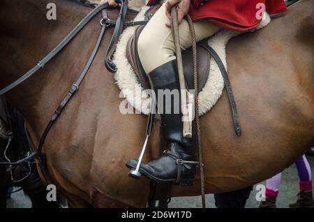 Nahaufnahme eines Jägers auf einem Pferd mit Stiefeln, Hosen und einem Teil des roten Mantels Stockfoto
