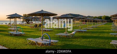 Reihen von Strohschirmen und Liegestühlen am Strand der Insel Rhodos, Griechenland Stockfoto