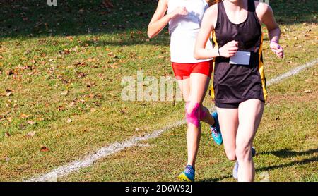 Zwei High School-Cross-Country-Läufer kämpfen während eines Rennens auf einem Grasfeld miteinander. Stockfoto