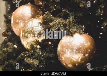 Bälle und Girlanden hängen an Kiefernästen vor festlicher Kulisse. Goldene Kugeln auf Fichte. Weihnachten Hintergrund. Stockfoto