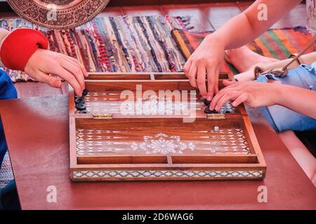 Das Spiel von zwei Leuten im alten Backgammon. Hände Spieler bewegen Chips auf dem Backgammon. Möbel im orientalischen Stil. Stockfoto