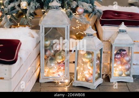 Laterne mit Weihnachtskugeln auf geschmücktem christbaumhintergrund im Wohnzimmer. Winterzeit und Lampe auf Holzsofa in der Nähe von weihnachtsbaum. Stockfoto