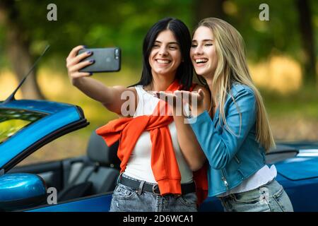Junge hübsche zwei Frauen Schlag Kuss nehmen ein Selfie während Stehen in der Nähe von Cabrio Auto auf der Straße Stockfoto