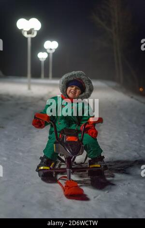 Junge auf Schneescooter in der Straße im Winter Abend Stockfoto