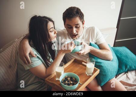Brunette Frau und ihr Liebhaber sitzen im Bett Fütterung Einander mit Getreide und Milch während eines Morgens verbracht Gemeinsam Stockfoto
