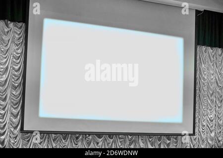 Reale Leinwand im Projektorraum, Konzept. Einziehbare flexible Leinwand für Videoübertragung. Leerer Bildschirm, um Filme auf der Bühne anzuzeigen. Stockfoto